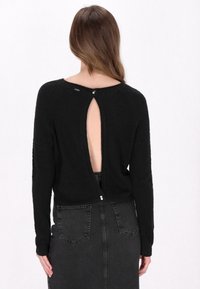 Pulover negru, texturat, cu mâneci lungi, design cu spate deschis fixat cu nasturi. Asortat cu o fustă din denim negru, cu talie înaltă.