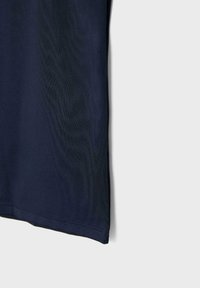 Granatowa tkanina o gładkiej fakturze z widocznym szwem na dolnej krawędzi na jasnoszarym tle.