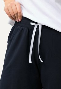 Pantaloni della tuta blu scuro realizzati in tessuto morbido, con cordoncino bianco, vita elastica e tasche laterali.