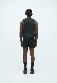 Schwarzes Sportweste mit elegantem Design, kombiniert mit schwarzen Shorts. Merkmale sind eine glatte Textur und eine taillierte Passform ohne sichtbare Logos.