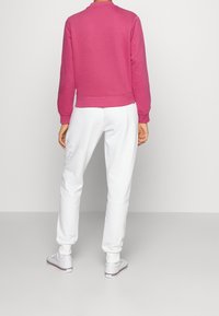 Fleece sweater in fel roze, met een geribde halslijn en manchetten. Gecombineerd met witte joggers met een subtiel logodetail en elastische manchetten.
