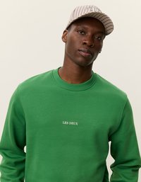 Žalias džemperis su apvaliu kaklu, išskirtinis balta "LES DEUX" užrašu priekyje. Suderintas su šviesių juostelių kepure.