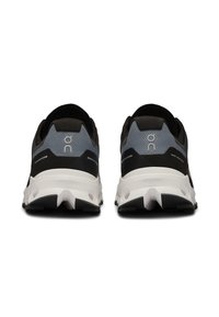 Zwarte en grijze sport schoenen met een gestructureerde bovenkant, een witte tussenzool en een zwarte buitenzool. Heeft branding op de hiel en reflecterende accenten.
