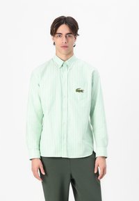 Green striped button-up shirt with collared neckline, long sleeves, and embroidered crocodile logo on the chest pocket. Cotton material.