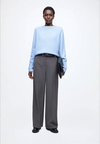 Jasnoniebieski dziany sweter z szerokim dekoltem, połączony z szarymi spodniami z wysokim stanem. Akcesoria obejmują czarną kopertówkę i buty.