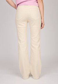 Pantalons évasés crème en tissu doux, dotés de poches arrière et d'une taille sans couture. Les jambes sont larges jusqu'à l'ourlet.