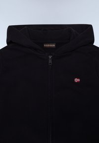 Sweatshirt noir à capuche zippée, avec un petit drapeau norvégien brodé sur la poitrine et une étiquette de marque au niveau du cou.