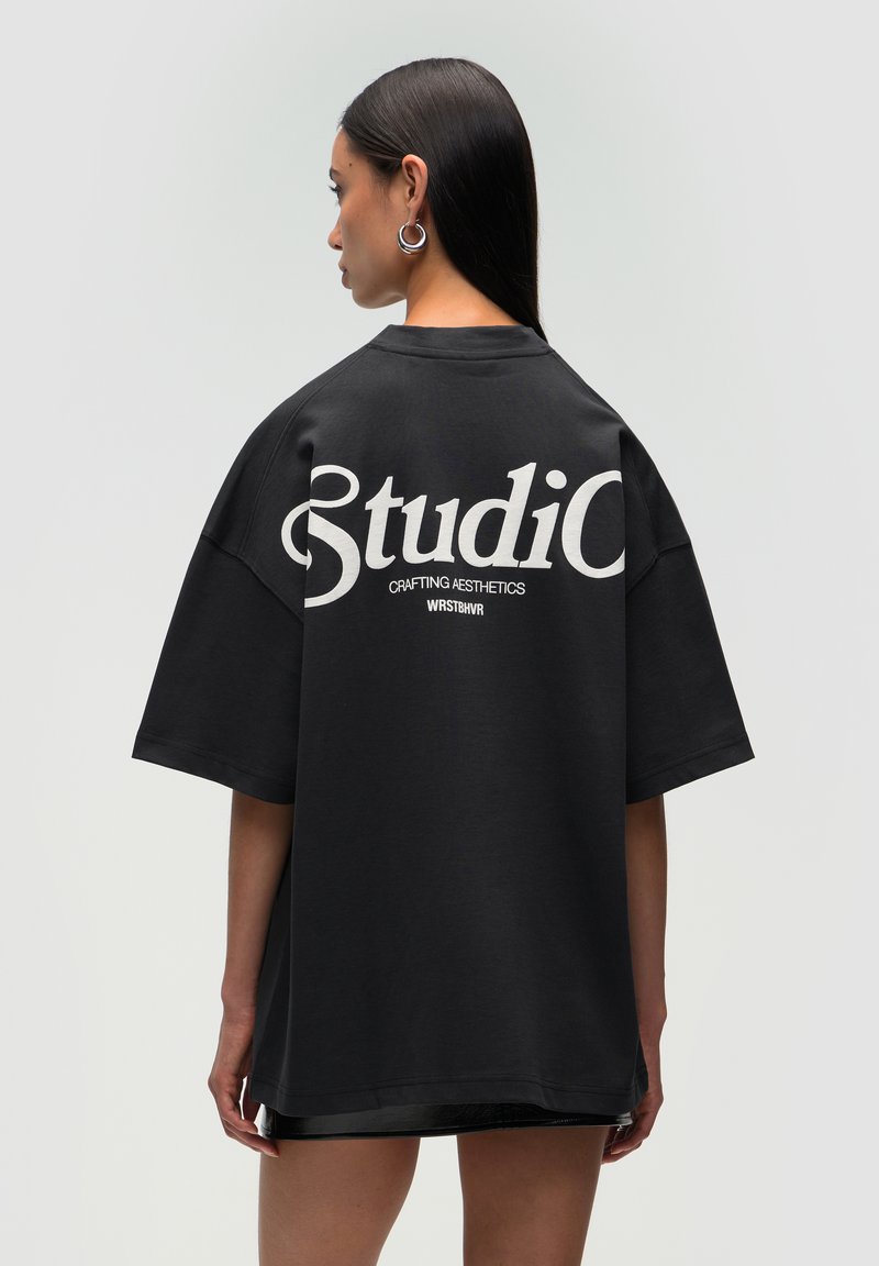 T-shirt noir surdimensionné avec un texte blanc au dos indiquant "Studio" et "Crafting Aesthetics". Tissu doux et coupe décontractée.