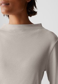 Hellbeige, geripptes Langarmoberteil mit hohem Kragen, das über eine weiche Textur und ein minimalistisches Design verfügt. Keine sichtbaren Muster oder Beschläge.