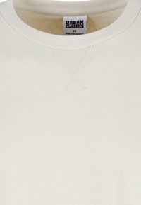 Sweatshirt beige deschis cu guler rotund, având un detaliu cu cusătură încrucișată pe piept și o etichetă cu textul "URBAN CLASSICS" în interiorul gulerului.
