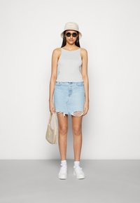 Top cinza, saia de ganga clara desbotada, tênis brancos, chapéu estilo bucket creme e óculos de sol, segurando uma bolsa bege. Textura suave.