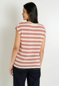 Top de punto con rayas horizontales rojas y blancas, mangas cortas, y un ajuste relajado, combinado con jeans azul oscuro. Material de mezcla de algodón texturizado.