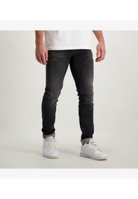 Donkerdenim jeans met een slim fit, voorzien van een vervaagde voorkant, opgerolde manchetten en een versleten textuur, gecombineerd met witte sneakers.
