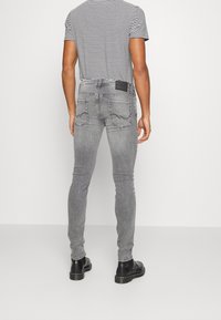 Vaqueros pitillo grises con textura desteñida, bolsillos traseros y una etiqueta de cuero negra. Combinados con una camiseta de rayas y botines negros.