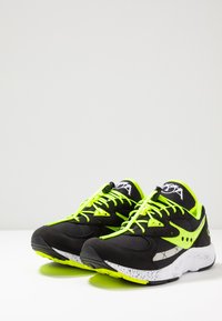Sneaker nere con accenti verde neon, caratterizzate da una tomaia in mesh e camoscio, dettagli riflettenti e una suola bianca maculata.