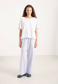 Balti per didelį t-shirt su plačiomis rankovėmis, derinama su šviesiai mėlynomis dryžuotomis plačiomis kelnėmis. Modelis vilki tamsius, tvirtus batus.