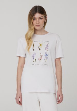 T-shirt bianco in cotone con un design grafico floreale in colori pastello e la scritta "JARDIN PARISIEN île-de-france 1993" in un carattere decorativo.
