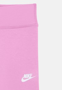 Rózsaszín edzőleggings széles derékpánttal, fehér Nike logóval a szegély közelében, egyszínű fehér háttéren.