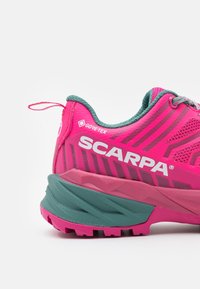 Der pinke SCARPA Trailschuh hat ein strukturiertes Obermaterial mit einem grünen Kragen, GORE-TEX-Logo und eine robuste Sohle für besseren Halt.