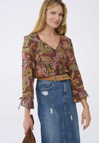 Bruine blouse met paisleyprint en roze en groene accenten, voorzien van een V-hals en ruchesmouwen, gecombineerd met een hoge taille spijkerrok.