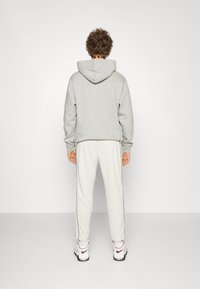 Grå kort hoodie med huva, kombinerad med ljusa joggers med svarta sidostrippar och vita sportskor.