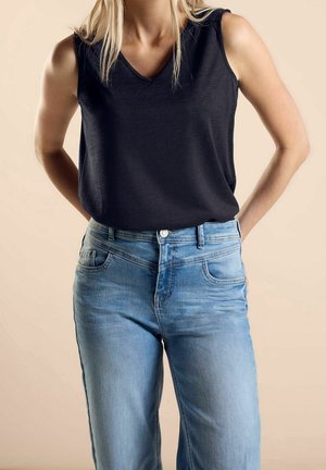 Sort ærmeløs top med v-hals, kombineret med lyseblå jeans med fem lommer og let falmet effekt. Glat stoftekstur.