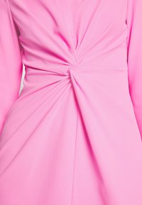 Robe rose avec un détail de nœud torsadé à la taille, faite d'un tissu doux au toucher lisse et dotée de longues manches.