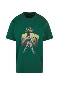 Grøn bomulds-T-shirt med et grafisk motiv af en spiller med udstrakte arme og teksten "The GREATEST" i fede gyldne bogstaver.