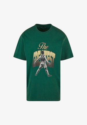 Zöld pamut póló, amelyen egy játékos látható, amint kinyújtott karokkal áll, és a "THE GREATEST" felirat szerepel vastag arany betűkkel.