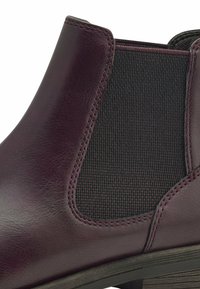 Gros plan d’une botte Chelsea en cuir violet foncé avec un panneau latéral élastique noir et des coutures visibles le long des bords.