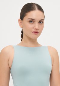 Body sportiv de culoare bleu deschis, cu o textură netedă, design fără mâneci și logo-ul Calvin Klein embosat pe față.