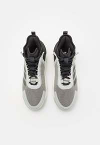Ett par grå och svarta atletiska sneakers med vita sulor, snörda framifrån, vy ovanifrån på en plain vit bakgrund.