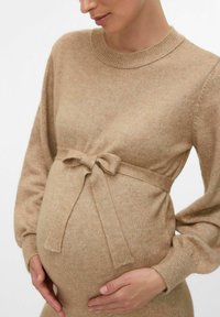 Abito in maglia premaman color beige con scollo rotondo, maniche lunghe e una cintura annodata che accentua la vita sopra una pancia arrotondata.