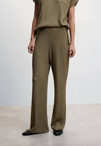 Tenue en maille olive avec un haut ample à motif texturé et un pantalon large, complétée par des ballerines noires.