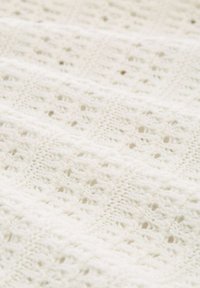 Gestrickter weißer Stoff mit einem Durchbruchs-Design, das quadratische und diamantförmige Muster zeigt, weiche Textur und zarte Details im gesamten Design.