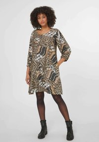 Schwarz-beiges gemustertes Kleid mit Dreiviertelärmeln, lockerer Passform und Taschen, kombiniert mit schwarzen Knöchelstiefeln. Glatte Stoffoberfläche.