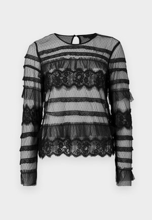 Haut noir à manches longues en tissu transparent, avec des accents en dentelle horizontale et des volants, et un détail de dos en trou de serrure. Motif à pois.