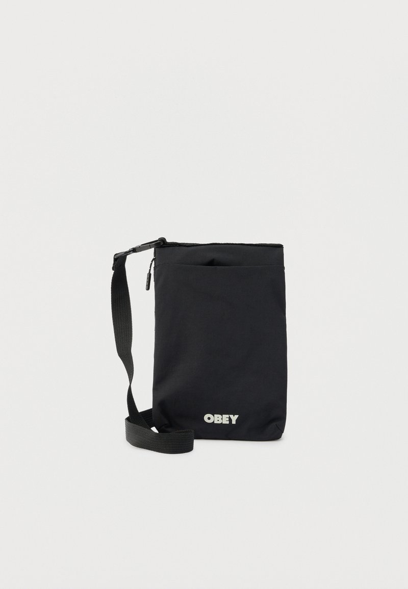Μαύρη τσάντα ώμου με ρυθμιζόμενο ιμάντα, κλείσιμο με φερμουάρ, μπροστινή τσέπη και το λογότυπο "OBEY" σε λευκό στο κάτω κέντρο.