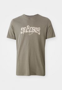 Olíva zöld pamut póló, középen stylizált fehér "Nike" logóval a mellkason. Rövid ujjú és kerek nyakú.