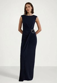 Tamsiai mėlyna, be rankovių maxi suknelė su drapiruotu dizainu ir grandinėlės akcentu ties juosmeniu. Glotni medžiaga sukuria elegantišką siluetą.