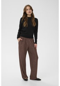 Fekete, hosszú ujjú pulóver és barna, csillogó, zsebes bő szárú nadrág. A nadrág sima textúrájú, áramló sziluettet alkot.