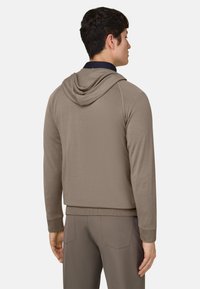 Sweat à capuche marron avec une finition texturée, doté d'une poche kangourou et de poignets côtelés. Vue de dos montrant un design élégant et décontracté.