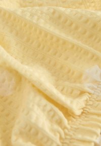 Tissu jaune doux avec un motif gaufré texturé et des bords frangés, présenté en plis doux.