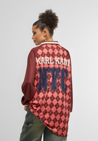 Raudonas ir rožinis argyle raštuotas per didelis marškiniai su baltu apykakle, ant nugaros su mėlyna spalva išspausdinti "KARL KANI" ir "NYC".