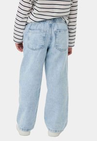 Vaqueros de denim azul claro con un ajuste relajado, cinturilla elástica y dos bolsillos traseros. Llevados con una camisa de manga larga a rayas.