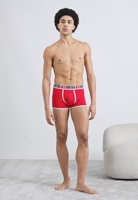 Sarkani kokvilnas bokseršorti ar melnu un baltu elastīgu jostiņu, uz kuras ir "DIESEL" logotips. Pieguļošs, vidēji garš līdz augšstilbiem.