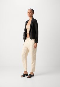 Svart blazer med en figursydd design, beige cropped topp, krämfärgade strukturerade byxor och svarta klacksandaler med blockklack. En enkel och modern estetik.