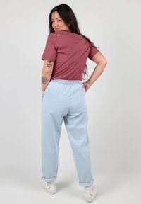 T-shirt à manches courtes bordeaux et joggers en denim bleu clair avec taille élastique, revers aux poignets et baskets blanches, montrés de dos.