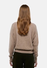 Pull en tricot beige avec une coupe décontractée, manches longues et ourlet côtelé. Texture douce, peu de détails au dos. Porté avec un pantalon noir.