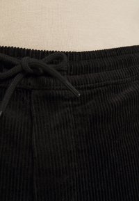 Zwarte corduroy broek met een koord in de taille, voorzien van verticale ribbels en een subtiele glans, met strikdetails op de tailleband.